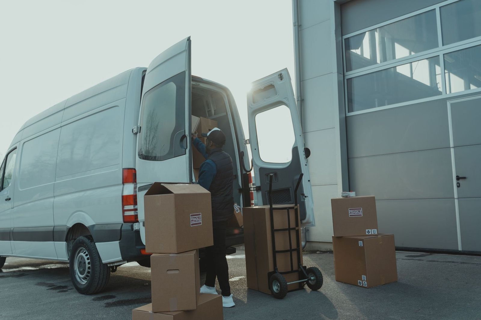 Repartidor cargando cajas en una camioneta de reparto frente a un depósito